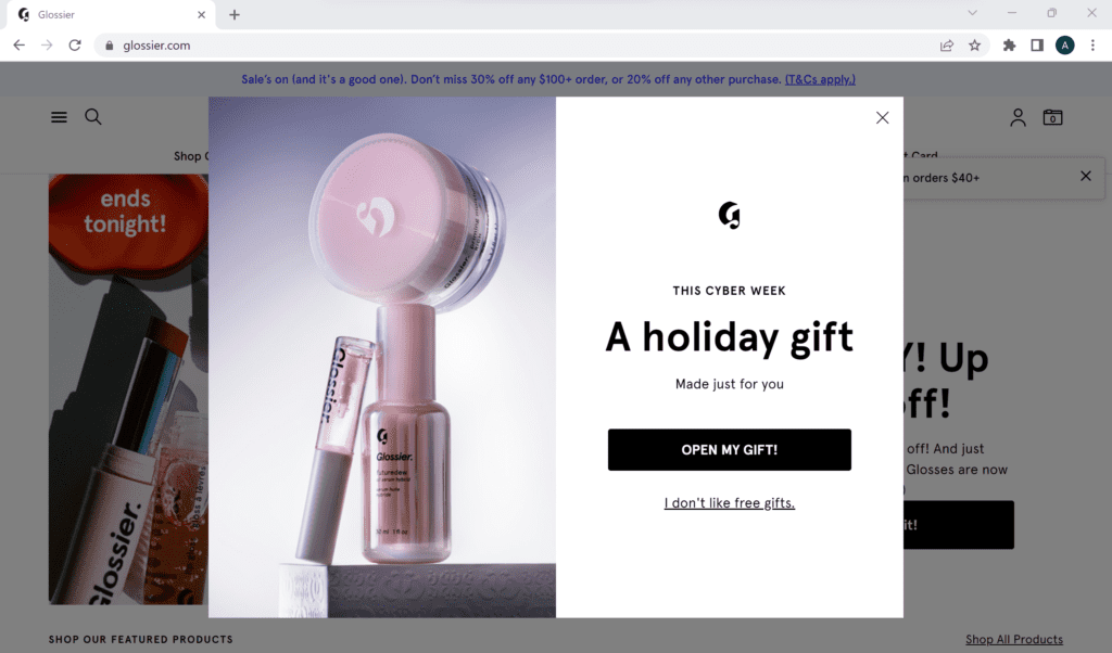 A website popup on Glossier saying "this cyber week, a holiday gift, made just for you" with a button saying "open my gift"